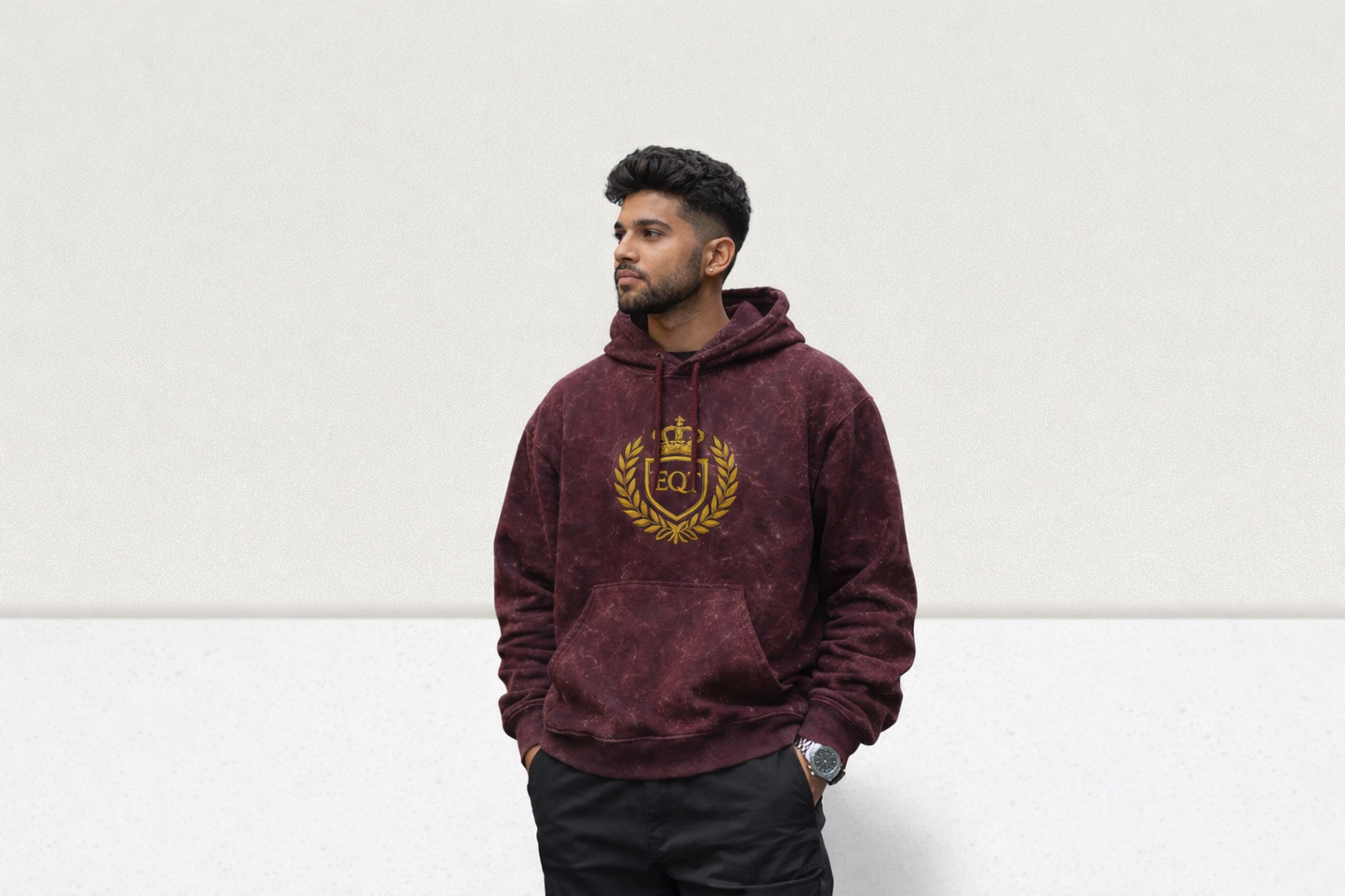 Man wearing a maroon hoodie with a gold emblem on a white background